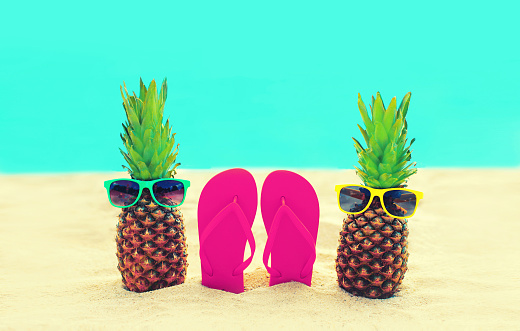 Summer vacation concept - pineapple with sunglasses and colorful flip flops on the beach on sea background