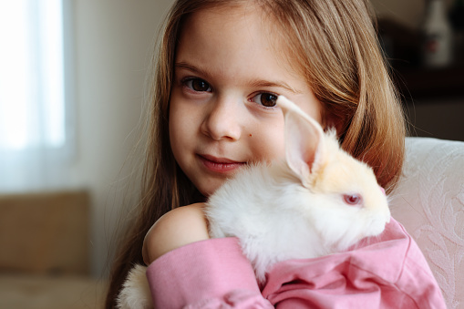 A close up portrait of a 6 year old girl hugging her pet rabbit.