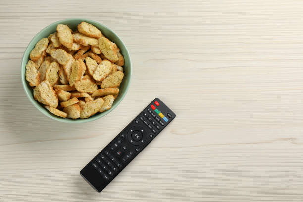 Modern tv remote control and rusks on white wooden table, flat lay. Space for text Modern tv remote control and rusks on white wooden table, flat lay. Space for text remote control on table stock pictures, royalty-free photos & images