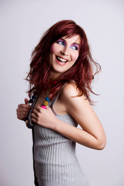 Horizontal studio shot on black of late teen girl with slight smile, both hands on hat.