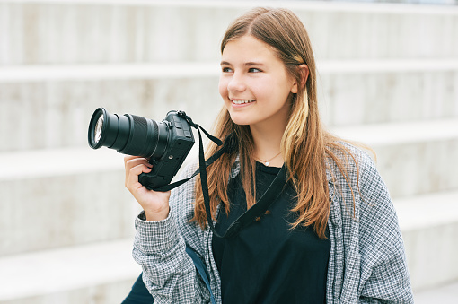 Outdoor portrait of young happy teenage girl holding mirrorless camera