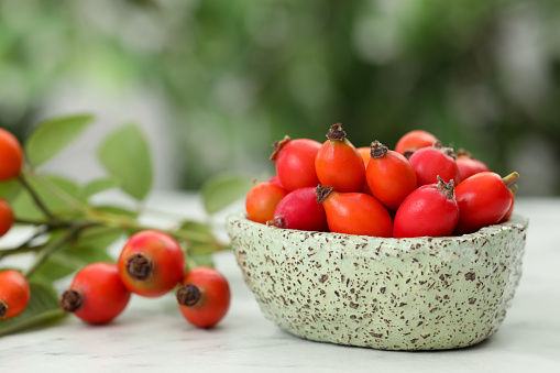 Ripe rose hip berries with green leaves on white wooden table outdoors, closeup. Space for text