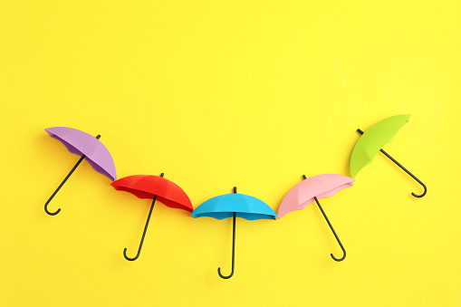 Bright toy umbrellas on yellow background, flat lay