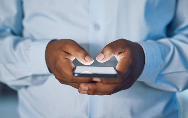 istock Closeup hands of african man using a phone while standing in his office. African american business man sending a text message while working late at night at his work. Putting in overtime after hours 1399178564