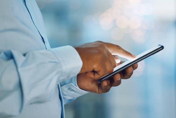 istock Closeup hands of african man using a phone while standing in his office. African american business man sending a text message while working late at night at his work. Putting in overtime after hours 1399178567