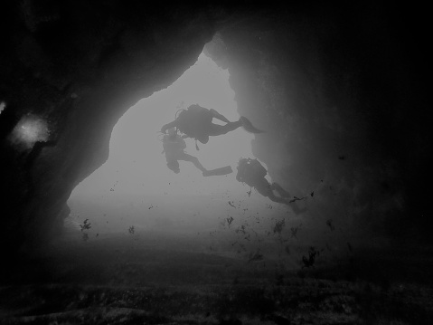 Three divers exiting a cave. Picture in black and white.  One diver is on his back to make sure the other ones are safe. The location is Tenerife, Canary Islands, Spain.