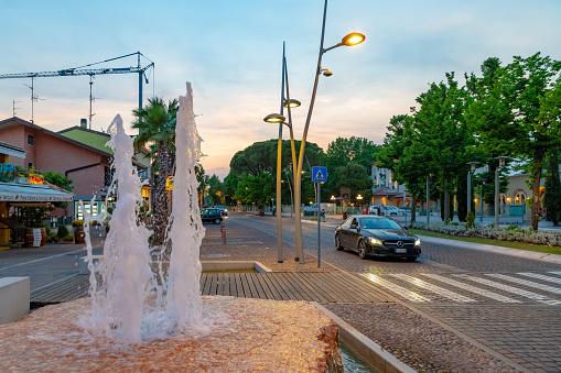 Main road through Sirmione on Lake Garda in Italy at sunset, fountain and a car passing.
