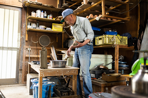 A senior Japanese man pottery master making cups in his workshop.