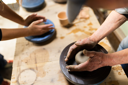 A close up of working hands in a pottery workshop crafting a mug.