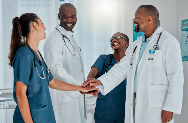 istock Group of happy diverse doctors stacking their hands together in support while working at a hospital. Medical professionals joining their hands in unity and motivation while working at a clinic 1399182380