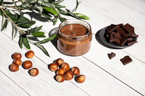 Jar of hazelnut butter, bunch of hazelnuts on white wooden table. Homemade hazelnut butter, natural, organic product. Modern wellness and vegan concept, raw food diet.