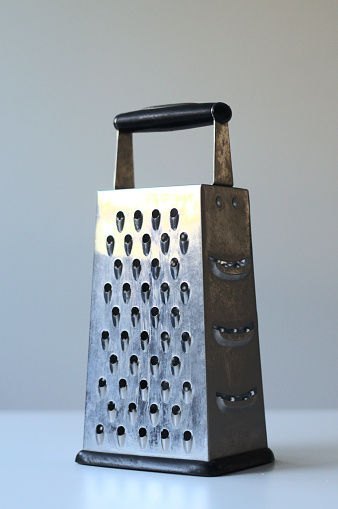 Close-up of grater on a white table with white background. It is not new and used already - you can see marks on a stainless steel of the grater.