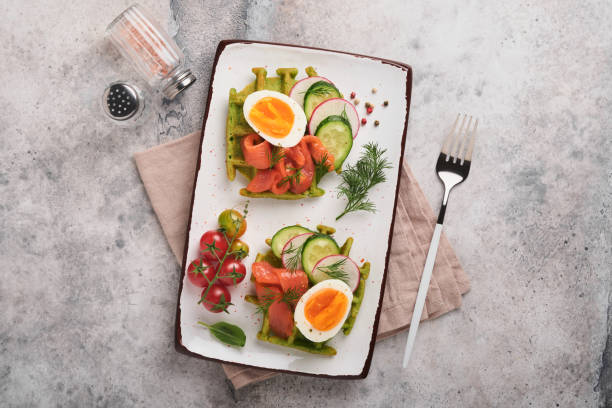 istock Savory waffles. Breakfast green waffles wild garlic or spinach with egg, tomato, salmon on plate for breakfast on grey concrete table background. Light dinner, lunch or breakfast. Top view. Mock up. 1399184842