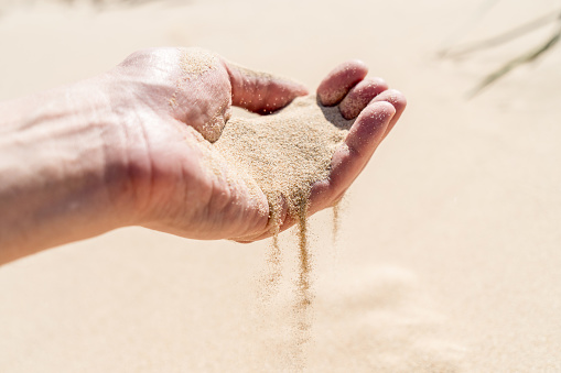 Sand spilling out pouring flow of the hand in the sandy desert dunes on bright sunny day. Transience of time. Selective focus