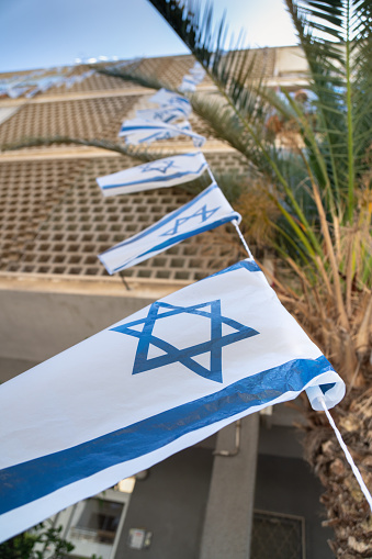 Israeli flags with star of David waving in the wind on a tight rope in front of windows of a residental building