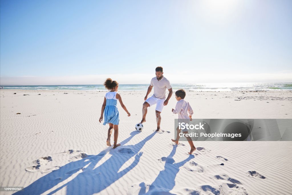 Carefree father and two children playing soccer on the beach. Single dad having fun and kicking ball with his little daughter and son while on vacation by the sea One Parent Stock Photo