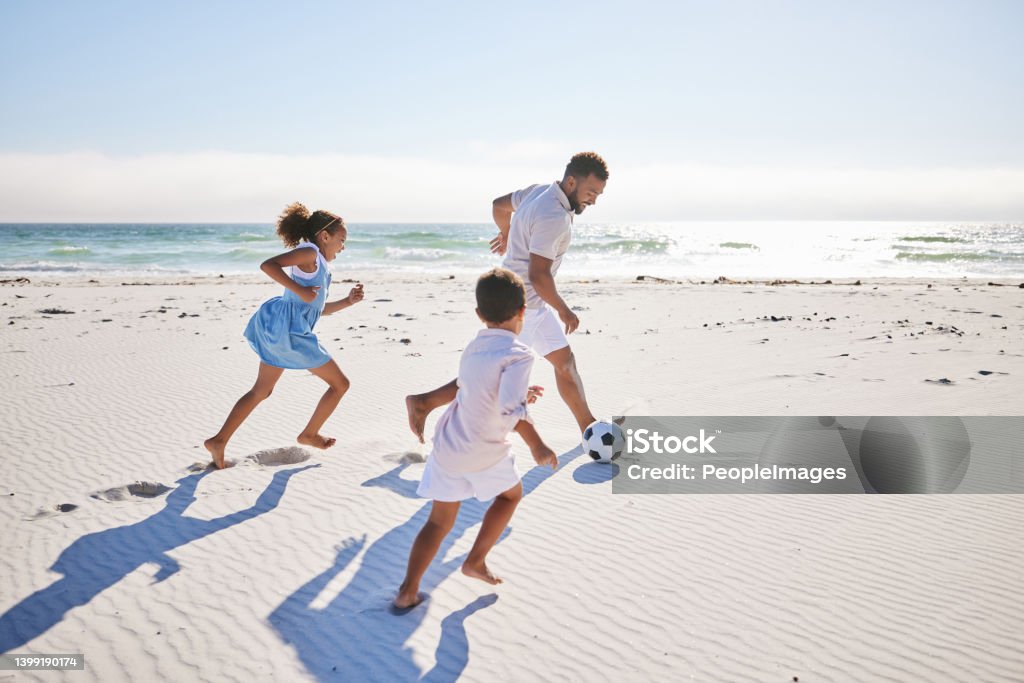 Healthy father and two children playing soccer on the beach. Single dad having fun and kicking ball with his daughter and son while on vacation by the sea Beach Stock Photo
