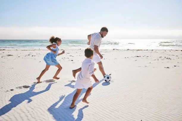 Photo of Healthy father and two children playing soccer on the beach. Single dad having fun and kicking ball with his daughter and son while on vacation by the sea