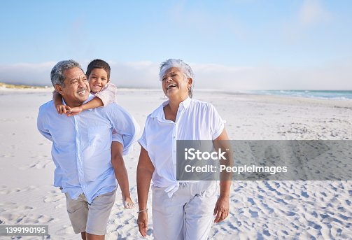 istock Happy mixed race grandparents walking on the beach with their grandson. Little boy enjoying a piggyback ride on his grandfathers back during summer vacation by the beach 1399190195