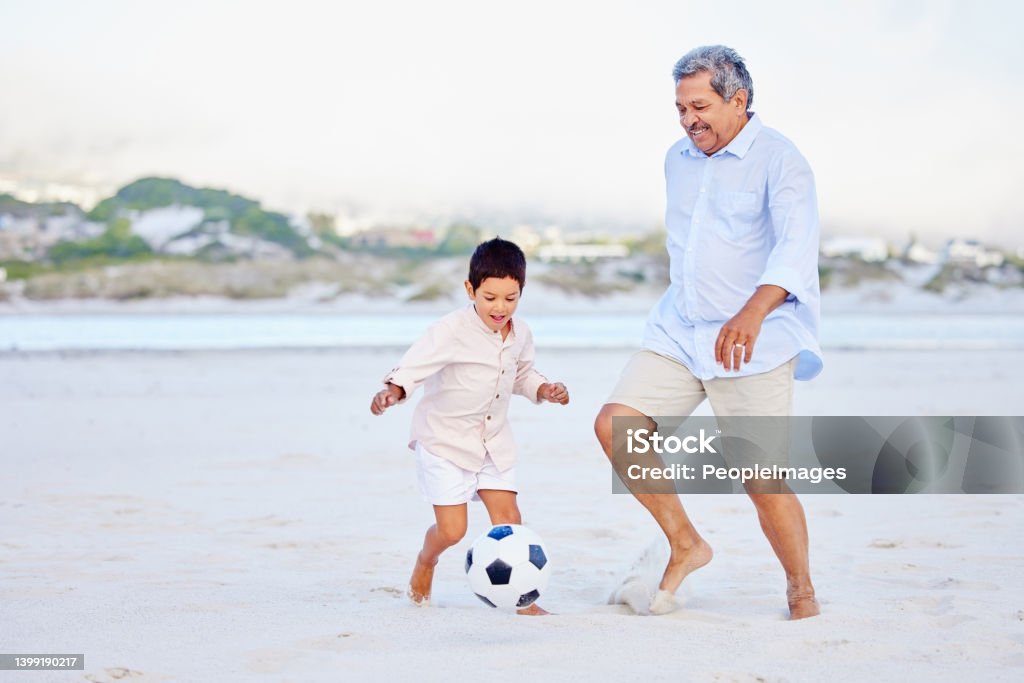 Active grandfather and grandson playing soccer on sandy beach. Cute little boy kicking ball with his grandpa Active Seniors Stock Photo