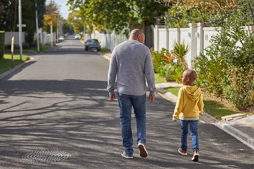Father and son walking in the street. Rear view of a mature man and his little boy going for a relaxing walk down the road and talking