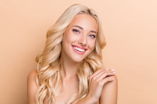 Portrait of attractive healthy cheerful wavy-haired girl touching shoulder scrub exfoliation isolated over beige pastel color background.