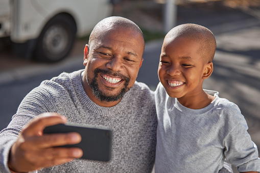 Father and son taking a selfie with a smartphone outside. A happy mature dad and his little boy having fun with a phone outdoors. Cute child enjoying family time