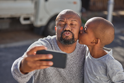 Father and son taking a selfie with a smartphone outside. A happy mature dad and his little boy having fun with a phone outdoors. Cute child enjoying family time