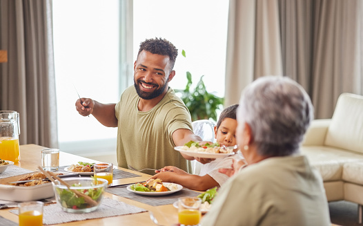 Closeup of a mixed race family having lunch at a table in the lounge at home and smiling while having a meal together