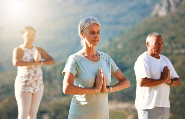 istock Three senior people meditating with joined hands and closed eyes breathing deeply. Multiethnic class of mature people doing yoga together in nature on a sunny day 1399195129