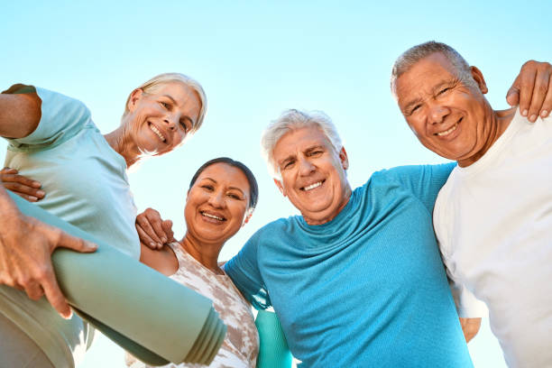 Portrait of a group of senior friends looking down at the camera while standing together. Smiling active senior people standing in a huddle after or before group yoga training in nature Portrait of a group of senior friends looking down at the camera while standing together. Smiling active senior people standing in a huddle after or before group yoga training in nature 50 59 years stock pictures, royalty-free photos & images