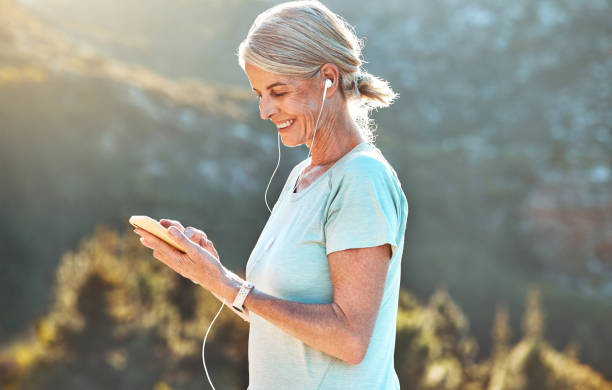 istock Active senior woman wearing earphones and using mobile app while out for a workout in nature on a sunny day 1399195177