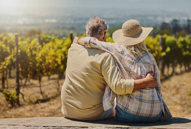 Rearview of unknown senior couple sitting with their arms around each other on their farm. Caucasian farmers bonding while admiring their vineyard and embracing. Elderly husband and wife hugging Rearview of unknown senior couple sitting with their arms around each other on their farm. Caucasian farmers bonding while admiring their vineyard and embracing. Elderly husband and wife hugging the farmer and his wife pictures stock pictures, royalty-free photos & images