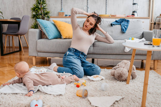 Young tired and sleepy mother sitting next to her crying baby boy on the floor in the living room.