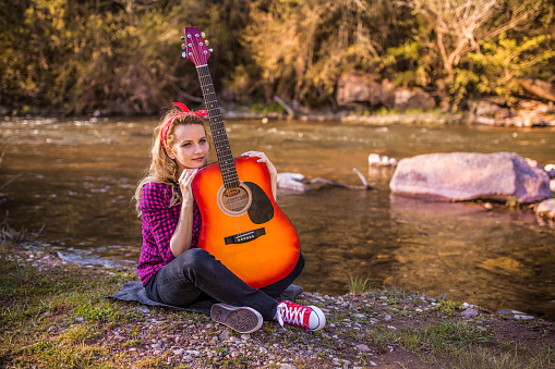 Young woman playing acoustic guitar on sunny day near the river