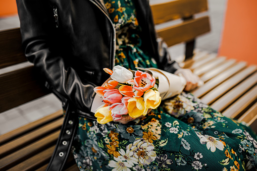 Close up of young woman sitting on park bunch and holding bouquet of tulips