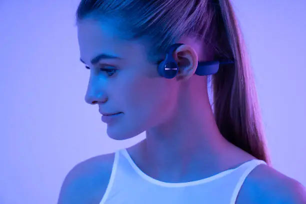 Photo of Beautiful woman in neon light wearing sport bone conduction headphones during fitness workout