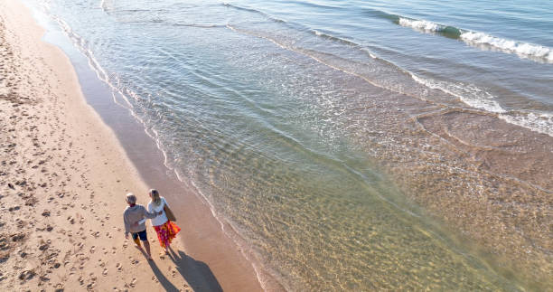 Aerial view of mature couple walking down sandy beach stock photo