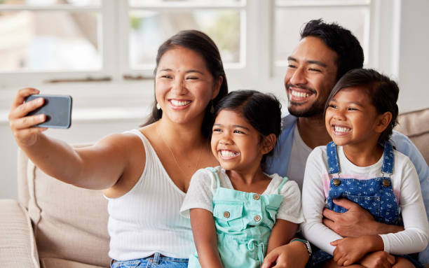 istock Smiling family using a cellphone to take a selfie together while smiling and looking carefree on the sofa at home 1399203767