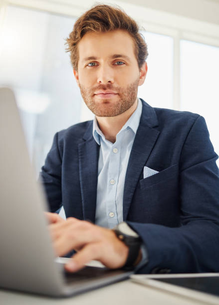 porträt eines fokussierten jungen kaukasischen geschäftsmannes, der an einem laptop in einem büro arbeitet. selbstbewusster und ehrgeiziger männlicher unternehmer, der im internet surft, während er an seinem schreibtisch an unternehmensplänen arbeite - compiling stock-fotos und bilder