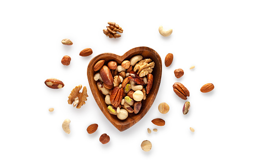 Various nuts in a wooden heart-shaped bowl on a white background