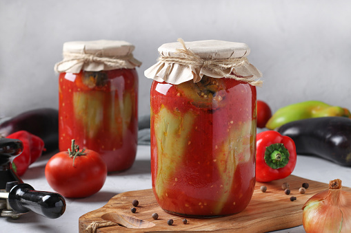 Peppers stuffed with eggplant and onions, in tomato sauce, in two glass jars on gray background