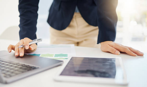 istock Closeup of one businesswoman writing notes while using a digital tablet device and laptop at a desk in an office. Hands of female entrepreneur browsing online while planning research documents and reviewing reports 1399206236