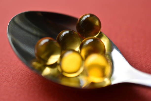 bolas amarillas con aceite de pescado sobre fondo rojo. bolas amarillas de vidrio. - capsule vitamin pill red lecithin fotografías e imágenes de stock