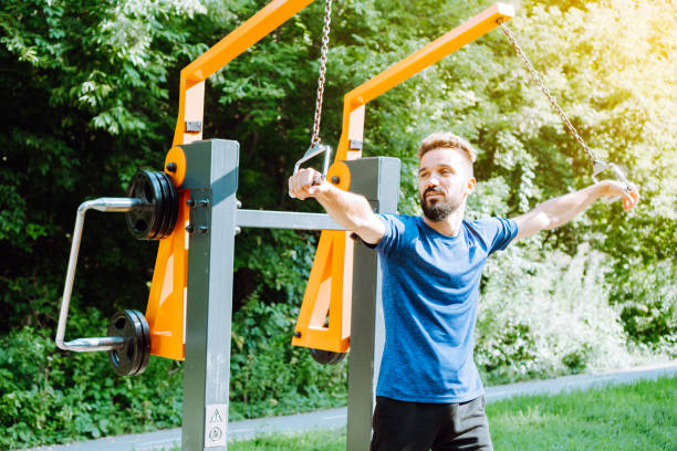 istock Chest workout with band crossovers. Charismatic man doing exercise on the outdoor exercise machine. Working out the pectoral muscles. 1399208717