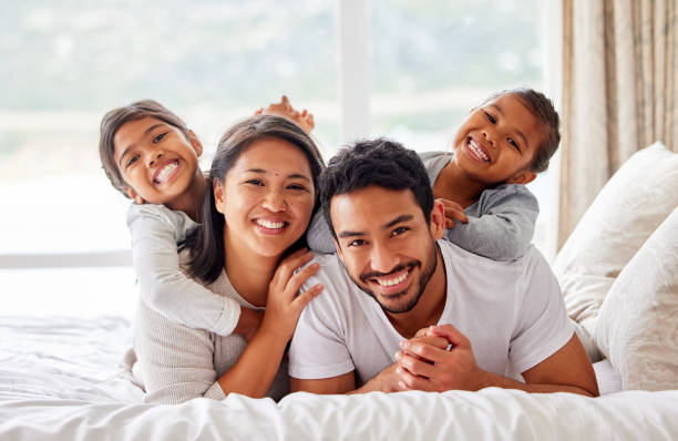 istock Young happy smiling couple looking cheerful and relaxed while sharing the bed with their daughters. Two girls being playful while in bed with their parents 1399208923