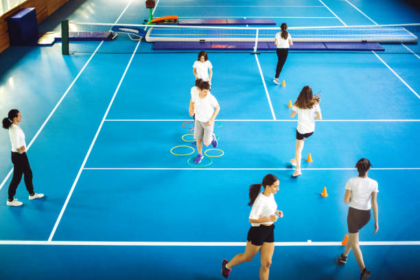 Group of teenage children doing plank exercise while trainer measuring a time in school gym
