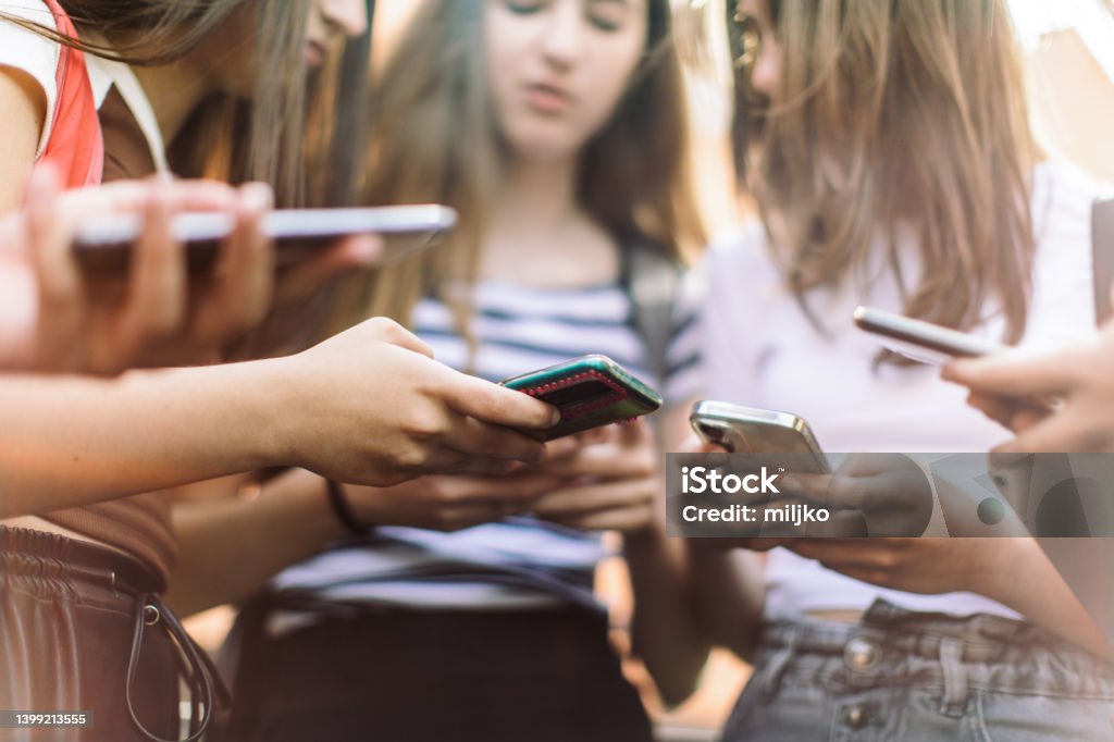 Teenage girls have fun and conversation using their mobile phones Group of teenage students standing in schoolyard and using mobile phones. They are very happy and playful. 14-15 Years Stock Photo