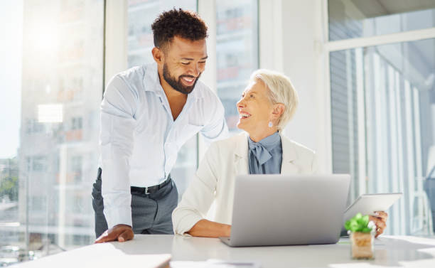istock Two happy diverse colleagues working together on a laptop and digital tablet device in an office boardroom. Young mixed race businessman meeting with mature caucasian businesswoman to discuss strategy plans and ideas 1399214880