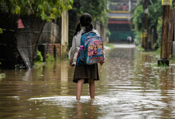 Waterlogging in India Guwahati, India. 25 May 2022.  A girl returns from school wades across a flooded street after heavy rains, in Guwahati. Waterlogging is a common scene in Guwahati city due to poor drainage system. climate change stock pictures, royalty-free photos & images
